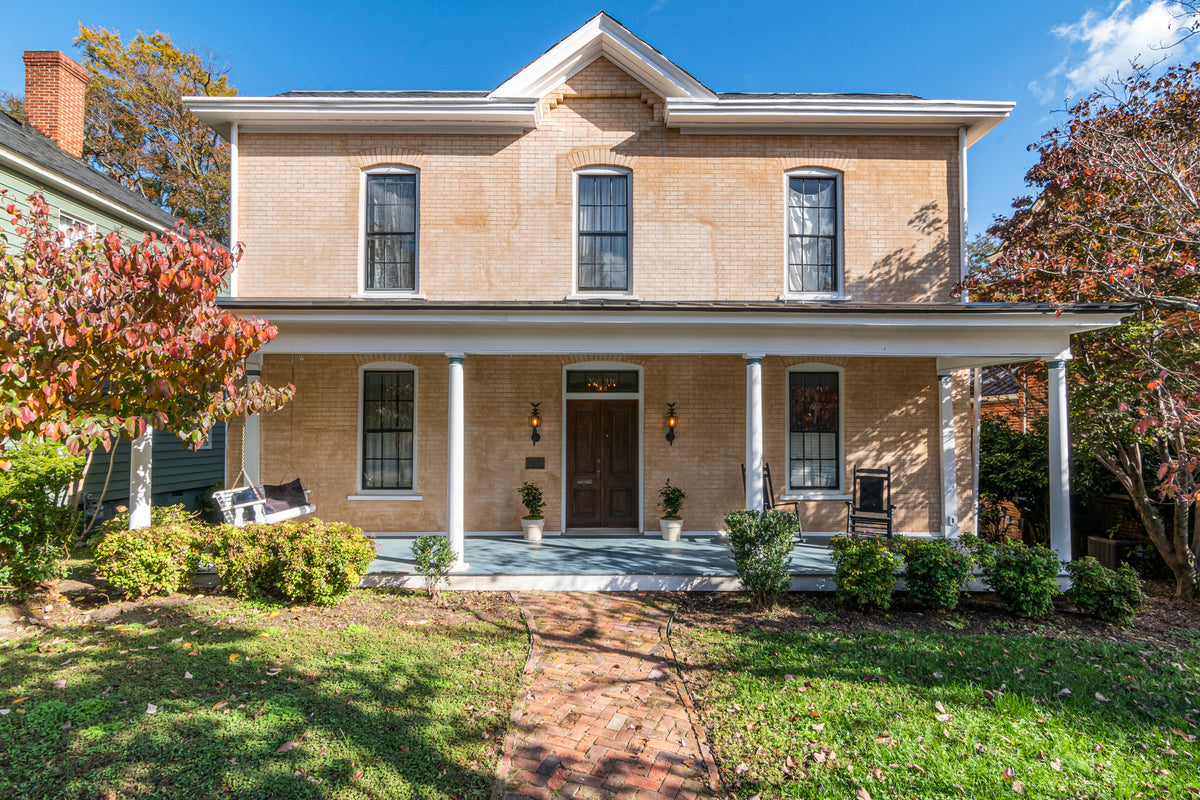 Original photograph of a tan brick home with five front windows, a central double door and a covered porch